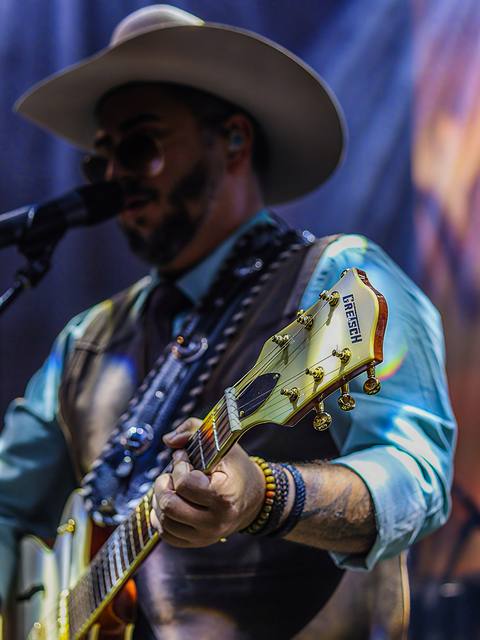Vocalista dos Folkadelicos de chapéu cantando com guitarra