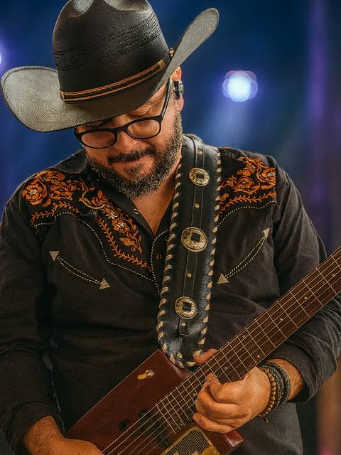 Guitarrista dos Folkadelicos de chapéu tocando sob luz azul